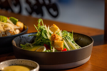 A vibrant salad with fresh greens, crispy toppings, and colorful vegetables served in a stylish black bowl on a wooden table.