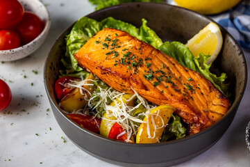 A beautifully plated salmon dish with fresh vegetables, garnished with herbs and lemon, served in a rustic bowl.