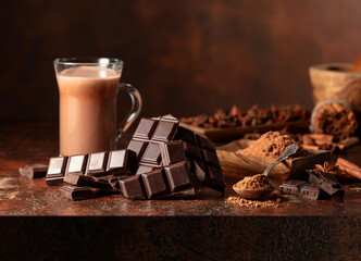 Pieces of bitter chocolate and glass of cocoa drink on a brown table.