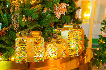 Christmas tree decorated with yellow gold balls and sparkling lights installed indoors, boxes gifts with gold satin silk ribbon for Christmas and New Year.