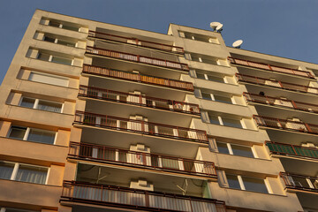 A tall highrise building featuring numerous balconies and various satellite dishes situated at its top, indicative of urban living standards