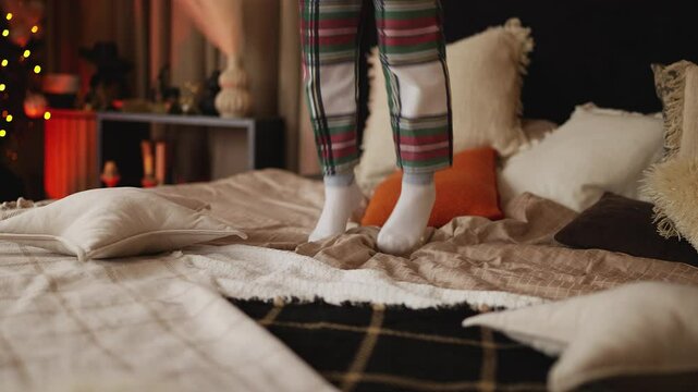 Child feet happily jumping on bed near Christmas tree, embracing winter holidays