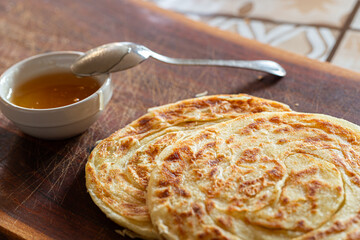 A plate of msemen on a wooden board, accompanied by honey in a white ceramic bowl and a silver spoon, offering a sweet Moroccan delight.