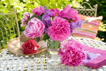 Pink peonies and roses in a glass vase on a metal table outdoors in a garden still life
