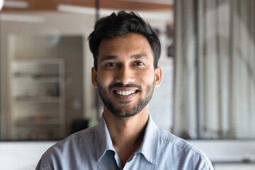 Head shot portrait millennial 30s Indian man dressed in casual blue shirt posing indoor. Profile picture of office employee, professional worker posing alone in creative field or business environment