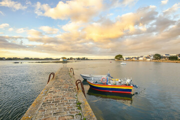 Pont qui avance au milieu de la mer avec des barques colorées amarrées et un ciel legerement...