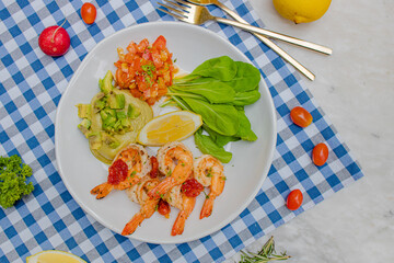 A colorful plate featuring shrimp, fresh vegetables, and lemon, set on a checkered tablecloth, evoking a vibrant and appetizing meal.