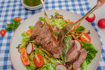 A vibrant salad topped with sliced steak, garnished with fresh herbs, served on a checkered tablecloth, creating a delicious and inviting meal.