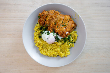 A plate of curry risotto with chicken katsu and egg.