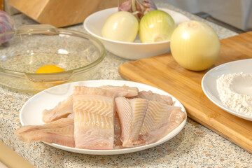 Sliced ​​pieces of fresh fish for further cooking against the background of onion heads and a...