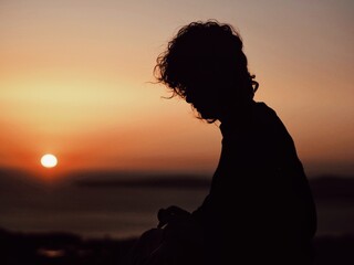The silhouette of a girl on top of a hill with the sea, the sunset and the sky in the background. 