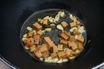 Golden-brown seitan cubes sizzling in a frying pan with garlic and olive oil. A healthy,...