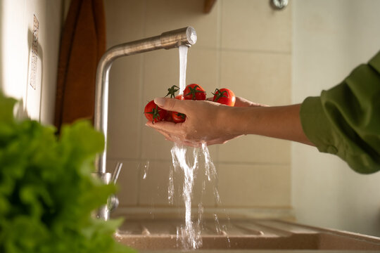 Hands are washing fresh vegetables in a modern kitchen, emphasizing cleanliness and preparation. The bright sink area enhances the cooking environment.