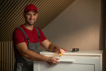 A skilled individual assembles a piece of furniture in a well-lit room. He uses various tools,...