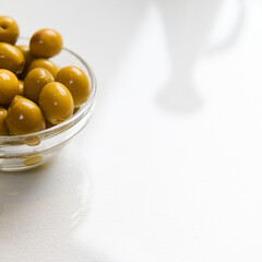 Glass bowl filled with green olives on a white background