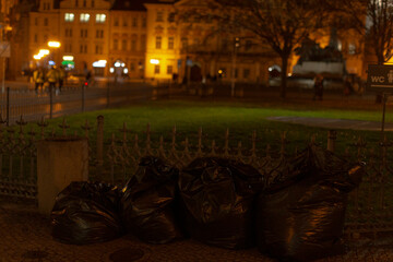 A large pile of garbage bags is visible in a park during the night, creating an unappealing sight under the limited lighting