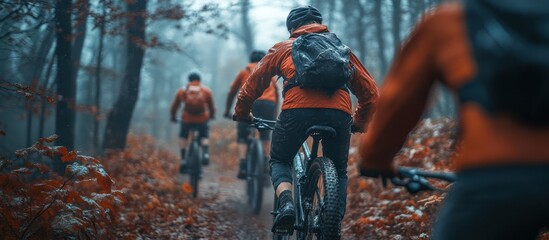 Three cyclists riding through a misty forest, wearing orange jackets.