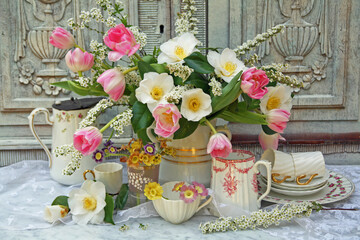 Spring flower still life with antique porcelain vases and jugs on a marble table with a wooden...