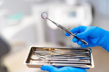 Dentist readies tools for patient exam. A dentist holds a dental mirror above a tray of instruments...