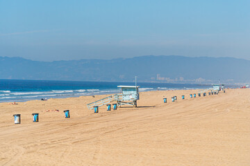 Obraz premium Californian beach near Los Angeles with typical lifeguard huts, tourists suntaning and garbage bins aligned on the sand