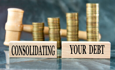 CONSOLIDATING YOUR DEBT - words on a wooden block on a background of stacks of coins