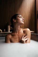 Asian young woman sitting in wooden bathtub is relaxing in hot spring. Relaxing in a natural hot bath. Selective focus. Foot bath at a Japanese open air hot spring, onsen. Skin care spa concept. 