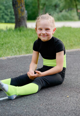 Fototapeta premium Sports and healthy childhood. Little girl does acrobatics and stretching exercises on playground in park.