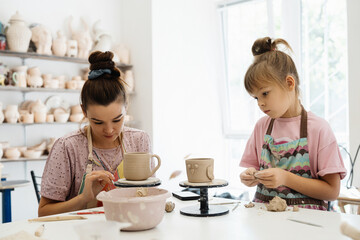 An adult and child create pottery together in a bright studio