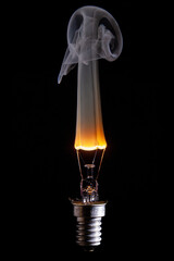gebrochene Glühlampe mit durchbrennender  Glühwendel, und rauchendem Wolframdraht vor schwarzen Hintergrund und komplett sichtbaren Lampengewinde E29