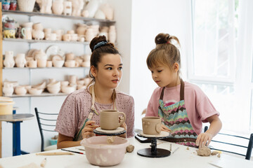 A pottery class where an adult teaches a child to shape clay in a studio