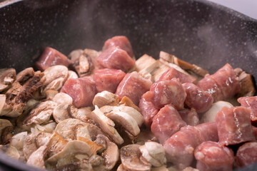 Cooking pieces of sausage and mushrooms in a frying pan.Fried food.Food concept.
