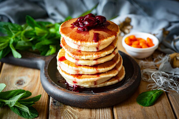 Delicious breakfast: A stack of pancakes with cherry syrup and cherries on a brown plate on a wooden table. Close-up
