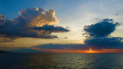 Clouds over the sea during sunset. View of cumulus clouds colored in warm colors by the rays of the setting sun over the surface of the ocean.
