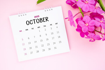 October 2025 desk calendar and pink orchid on pink color background.