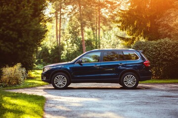 Fototapeta premium Dark blue SUV parked on a gravel road in a sunny forest setting.