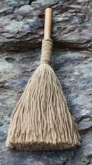A rustic broom lies on a stone surface, showcasing its natural fibers and craftsmanship