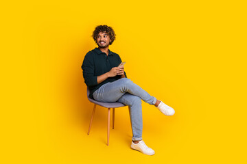 Young man holding phone on modern chair against vibrant yellow backdrop