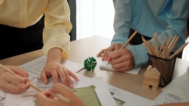 Smart architect and safety engineer discussion about building blueprint on table with architectural document, measurement tools and wooden block scatter around at modern office. Closeup. Delineation.