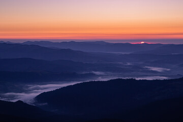 Obraz premium dawn on the top of the mountain, the sun peeks out, the fog hides in the lowlands