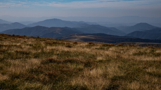 foggy morning high in the mountains in autumn, dry yellow grass in the foreground and mountain ranges in blue haze stretching to the horizon