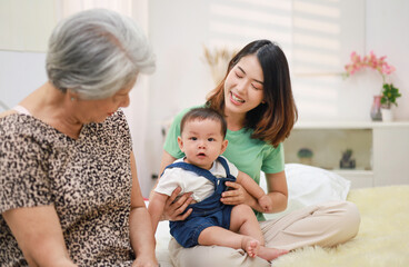 Family concept, smiling mother, baby son and grandmother sitting together at home.