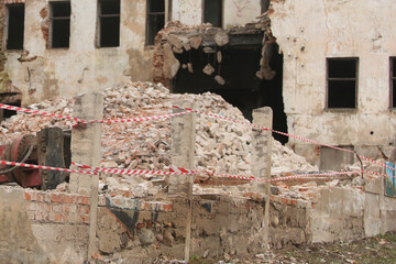A building being demolished, surrounded by broken bricks and construction equipment. The area is...