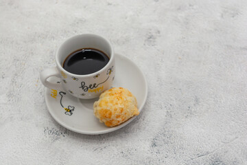 Brazilian cheese bread paired with a cup of black coffee on a decorative saucer.