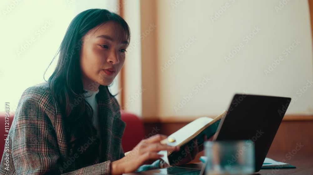 Poster young professional woman works remotely, taking notes in a notebook while engaging in a video call o