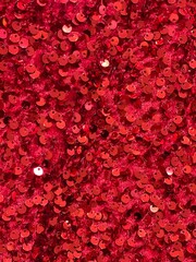 Seamless red fabric texture with sequins. Sequin fabric texture. Shiny red sparkling background. Clothing piece of glitter metallic for a glamorous party, celebration. Close-up.