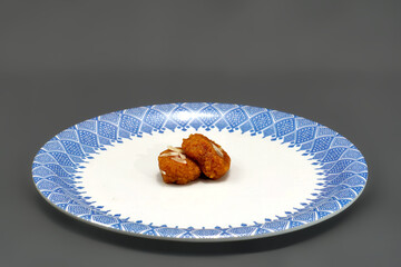 Patterned white plate holds two pieces of a classic Gujarati sweet Mohanthal