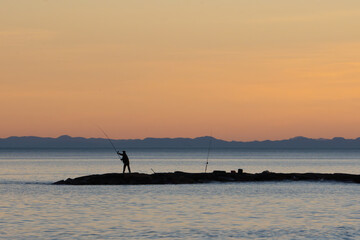 Silhouette of a fisherman picking up fishing line while fishing by the Mediterranean Sea on a wave...
