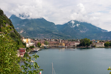 Fototapeta premium Panoramic view of idyllic lakeside town Riva Del Garda at lake Garda, Trentino, Northern Italy. Surrounded by majestic cloud covered mountains of Garda Hills. Colorful houses at harbor. Summer travel