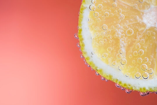 Close-up of a slice of lemon in soda water against a pink background