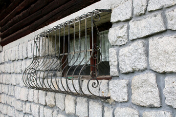 Finestra con inferriata sporgente in ferro battuto su facciata di pietra e legno